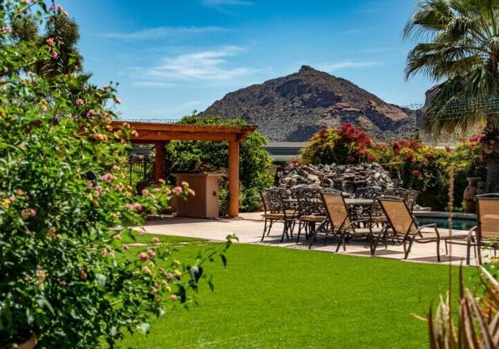 Lush backyard with wood pergola, outdoor dining set, pool, rock water feature, and dramatic mountain backdrop