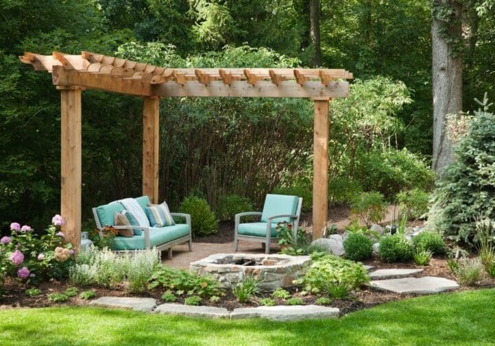 Cedar pergola with stone fire pit, teal cushioned seating, hydrangea blooms, and lush garden surroundings