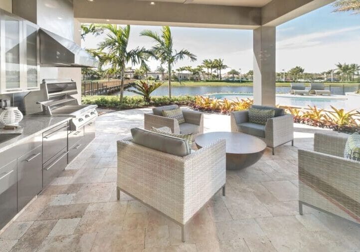 Luxury covered patio with modern outdoor kitchen, wicker lounge seating, and waterfront palm tree views