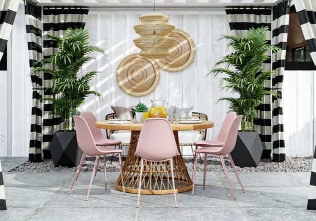 Stylish outdoor dining area with a rattan table, pink chairs, tropical plants, and black-and-white striped curtains