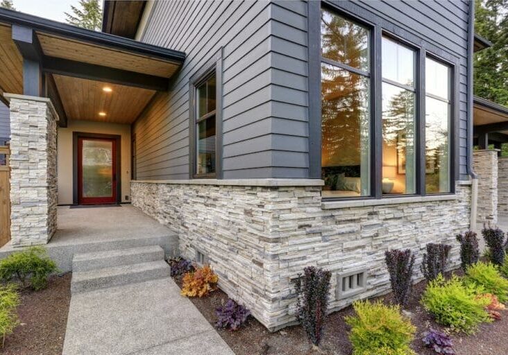 Modern home exterior with stone veneer siding, red front door, and decorative landscaping