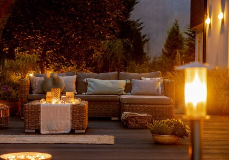 Cozy evening deck with wicker sectional sofa, candlelit coffee table, and warm outdoor lantern lighting