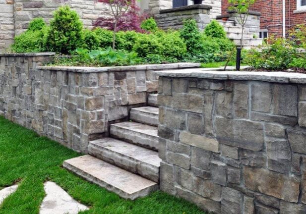 Natural stone retaining wall with built-in steps supporting a raised garden bed in a luxury landscape.